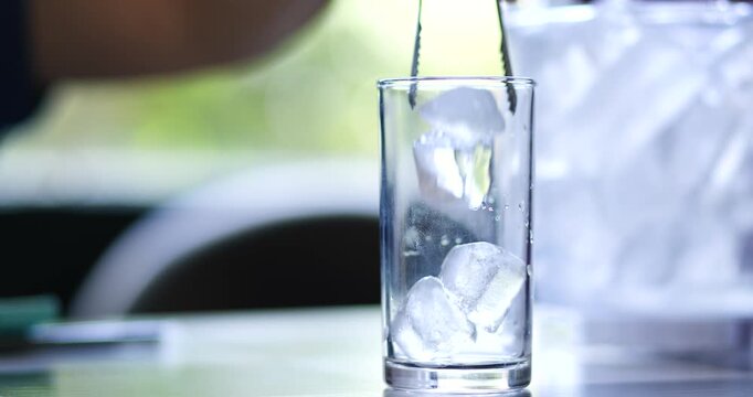 Hand using tongs to place ice cubes into a glass from an ice bucket. Beverage preparation, Bar service, Refreshment, Hospitality and food service concepts, close-up