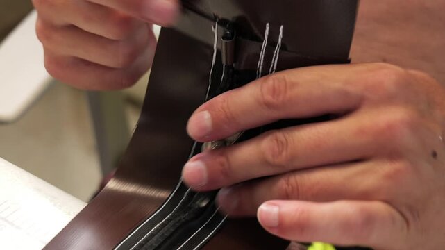 Professional tailor hand sewing a zipper onto brown fabric