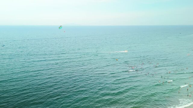 My khe beach in da nang. Vietnam. Showing a colorful parasail with a person in the air. A speedboat below leaving a wake on the vast turquoise ocean. And distant mountains under a bright sky