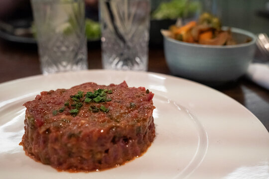 tatar wołowy na białym talerzu z gotowanymi warzywami podanymi osobno w restauracji
