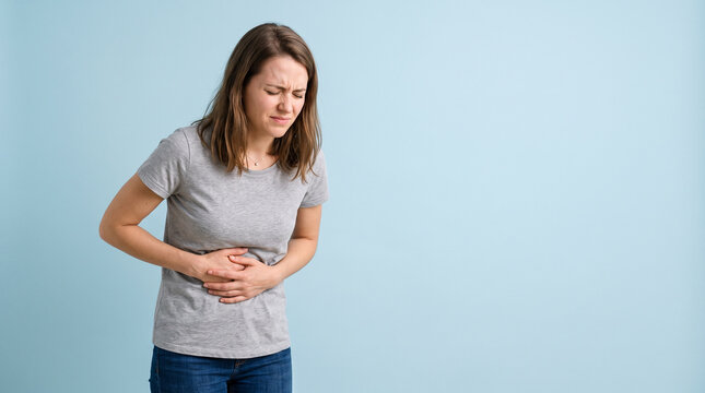 Young Woman Experiencing Abdominal Pain and Stomach Cramps Standing Against Blue Background