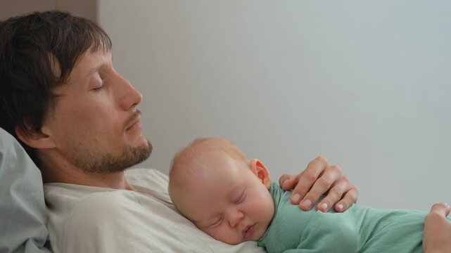 Swaddled baby son sleeping on father's belly on bed.