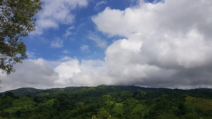 Obraz premium Breathtaking View of Lush Green Tropical Mountains Beneath a Vast Blue Sky with Soft White Clouds on a Sunny Day