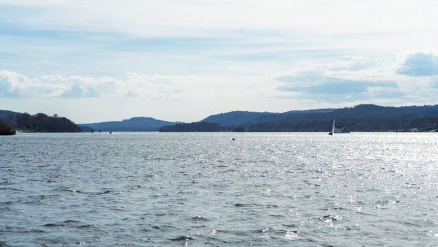 Lake Windermere in the Lake District National Park, where a small white sailboat is visible on the water, along with a ferry or pleasure boat on the right