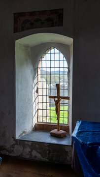 A window of an old church with a semicircular or Gothic arch and a wooden crucifix on the stone sill