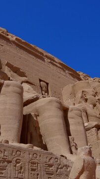 Close-up of giant Ramesses II colossi carved into rock facade at Abu Simbel temple, Egypt. Dramatic upward view of ancient sandstone pharaoh statues. Travel and history.