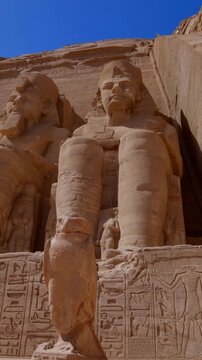 Close-up of giant Ramesses II colossi carved into rock facade at Abu Simbel temple, Egypt. Dramatic upward view of ancient sandstone pharaoh statues. Travel and history.
