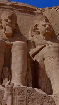 Close-up of giant Ramesses II colossi carved into rock facade at Abu Simbel temple, Egypt. Dramatic upward view of ancient sandstone pharaoh statues. Travel and history.