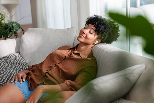 Woman relaxing on couch with wireless earbuds and closed eyes