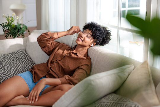 Woman relaxing on couch with earbuds, smiling.