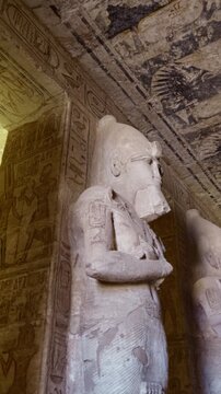 Grand hypostyle hall of Abu Simbel temple, Egypt, with two rows of colossal Ramesses II osiride figures flanking painted ceiling covered in vultures, cartouches and hieroglyphics.