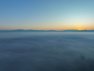 Obraz premium aerial view a sea of white mist envelops the mountain peak, slowly flowing down from the mountain peak. The mist poured down from the mountains in the morning. the sea of mist background.
