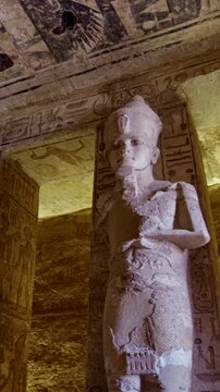 Grand hypostyle hall of Abu Simbel temple, Egypt, with two rows of colossal Ramesses II osiride figures flanking painted ceiling covered in vultures, cartouches and hieroglyphics.