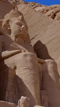 Close-up of giant Ramesses II colossi carved into rock facade at Abu Simbel temple, Egypt. Dramatic upward view of ancient sandstone pharaoh statues. Travel and history.