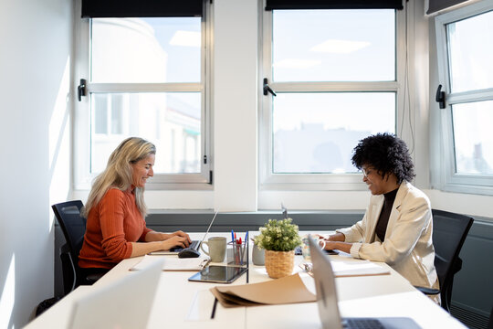 Businesswomen collaborating on laptops in modern office
