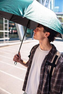 Young man with umbrella looks toward the city.