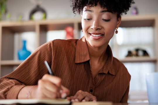 Woman writing in notebook, smiling, wearing brown shirt.