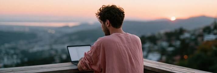 Fototapeta premium Young man using laptop at dusk overlooking coastal city for remote work banner and inspirational background wallpaper
