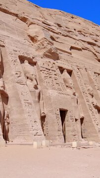 Monumental rock-cut facade of the Nefertari Temple with colossal statues and hieroglyphs under clear blue sky, showcasing ancient Egyptian architecture and grandeur.