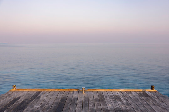Wooden jetty over a calm vast sea at sunrise