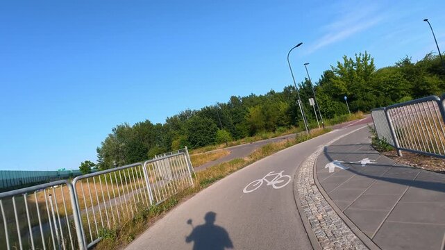 Bicycle and pedestrian path curving along noise barrier in suburbs. POV bicycle ride, sharp turn