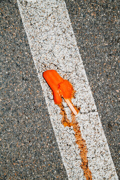 a dropped orange ice pop melts across a road marking
