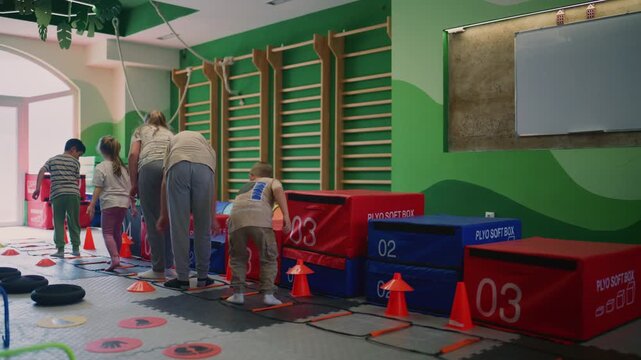 Young children participate in an agility fitness training session inside a vibrant gym. They are actively engaged in various physical exercises and movements guided by an instructor.