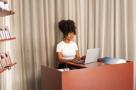 Smiling Receptionist Working on Laptop at Modern Salon Front 