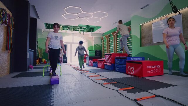 Young children and adults participate in a range of fitness exercises and agility training in a colorful indoor gym.