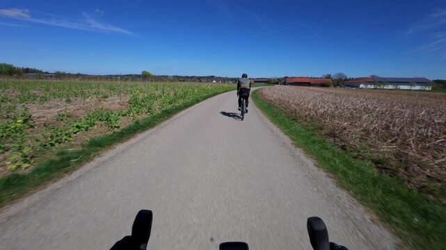 Bicycle point of view footage following a cyclist from the back on a scenic asphalt road through lush green countryside in Bavaria during spring season capturing an active outdoor training ride