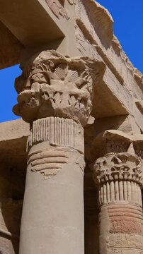 Dramatic upward view of ornate papyrus columns with carved floral capitals and stone lintels at Philae temple, Aswan, Egypt, against vivid deep blue sky.