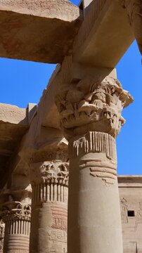Dramatic upward view of ornate papyrus columns with carved floral capitals and stone lintels at Philae temple, Aswan, Egypt, against vivid deep blue sky.