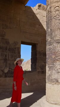A woman in a red dress examines the ruins of the Philae Temple, Aswan, Egypt.