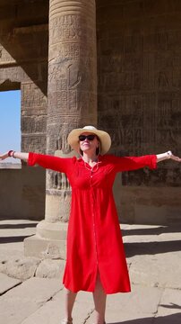 A woman in a red dress examines the ruins of the Philae Temple, Aswan, Egypt.