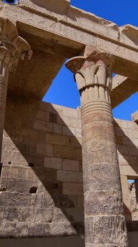 Dramatic upward view of ornate papyrus columns with carved floral capitals and stone lintels at Philae temple, Aswan, Egypt, against vivid deep blue sky.