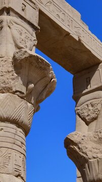 Dramatic upward view of ornate papyrus columns with carved floral capitals and stone lintels at Philae temple, Aswan, Egypt, against vivid deep blue sky.