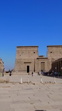 Tourists exploring the Philae Temple complex under clear blue sky, showcasing ancient Egyptian architecture, courtyards, and well-preserved stone structures.