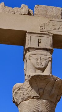 Upward view of ornate floral capitals on Ptolemaic columns at Philae Temple, Aswan Egypt. Elegant ancient architecture against vivid blue sky. Travel and history content.