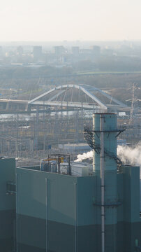Aerial view of Vattenfall Elektriciteitscentrale Diemen with its prominent chimney and industrial facilities, featuring a large arch bridge and urban skyline in Diemen, Noord-Holland, Netherlands.