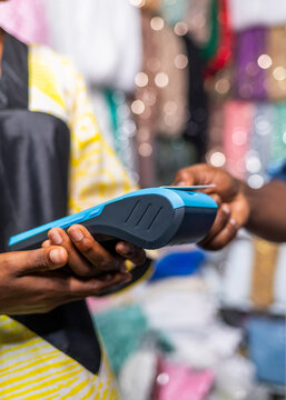 African businesswoman processing credit card payment using pos terminal in her fabric garment shop