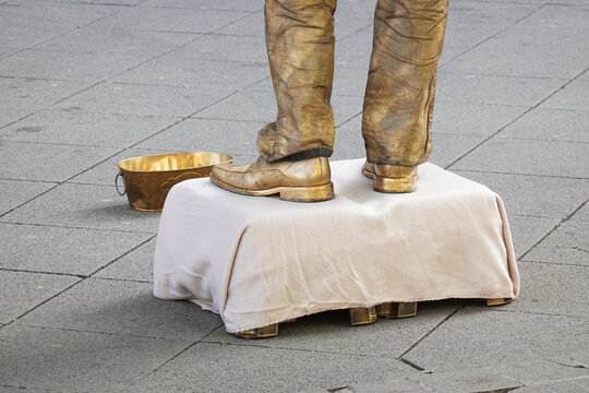 Living statue street artist painted gold performs on city street with golden bucket