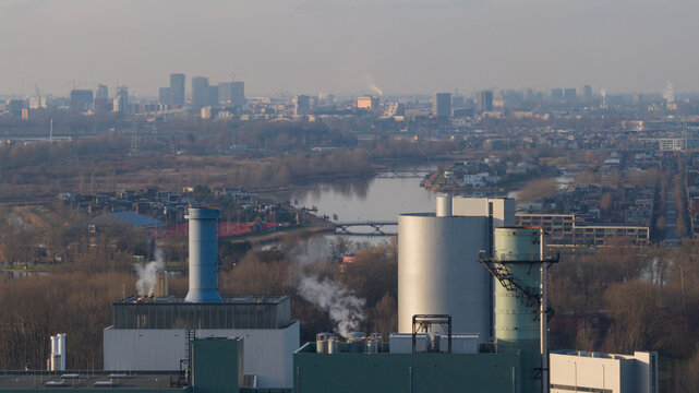 Aerial view of Vattenfall Elektriciteitscentrale Diemen with industrial chimneys emitting smoke, surrounded by trees and a river, in Diemen, Noord-Holland, Netherlands.