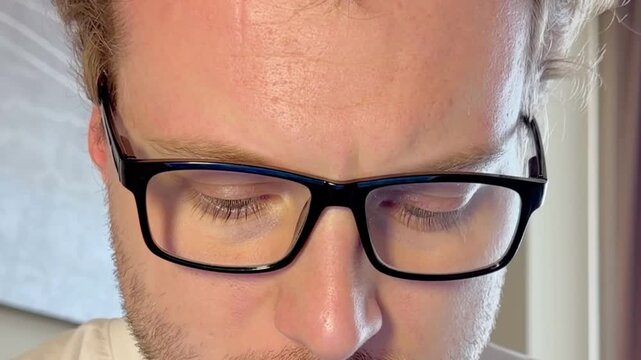 Close-Up of a Young Man Working on a Laptop, Wearing Glasses with the Screen Light Reflecting in His Lenses