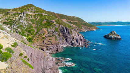 Fototapeta premium Aerial view of the dramatic rocky coastline and cliffs near Nebida, featuring the Spiaggia di Fontanamare in the distance, Sardinia, Italy