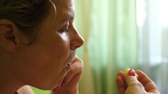 Side close-up of a woman eating a corn puff snack. Natural light snack moment near a window with soft daylight.