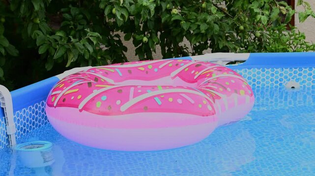 A pink inflatable donut float drifts gently on the clear blue water of a backyard swimming pool.