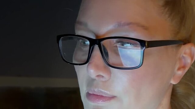 Woman Working Late at Night on a Laptop with the Blue Glow of the Screen Illuminating Her Face and Glasses