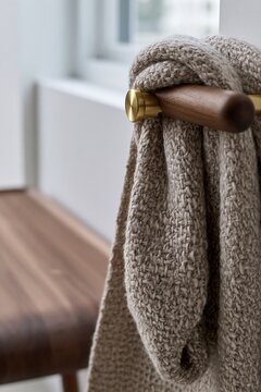 Cozy knitted blanket draped over wooden rail with brass accent, minimalist Scandinavian interior