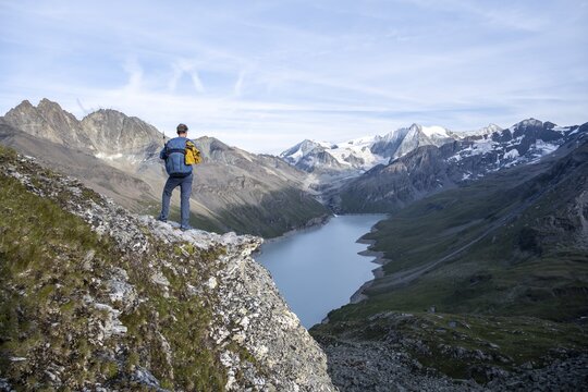 Mountaineer on the summit of Mont de la Blana, view of a blue mountain lake, Lac des Dix reservoir, behind mountain peak Mont Blanc de Cheilon with glacier, H&eacute;rm&eacute;nence, Valais Alps, Valais, Switzerland