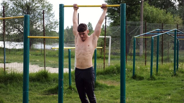 Muscular athlete doing pull ups on horizontal bar at sports ground. Young shirtless sportsman exercising at nature. Strong sporty man training outdoor. Concept of healthy and active lifestyle. Slow mo